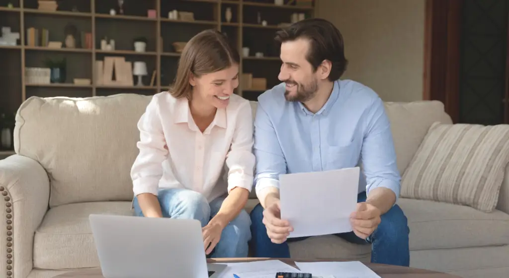 Smiling couple sits on a couch with a laptop and papers, appearing to review documents together. - Jeannie’s Cleaning Company - Jeannie’s Cleaning Company Smiling couple sits on a couch with a laptop and papers, appearing to review documents together.